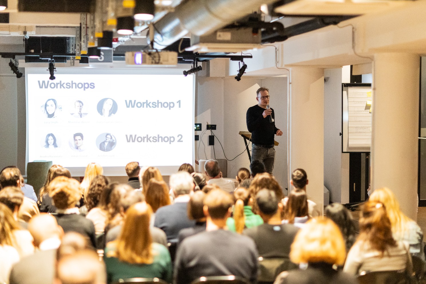 A speaker presents the workshop line-up to a full room